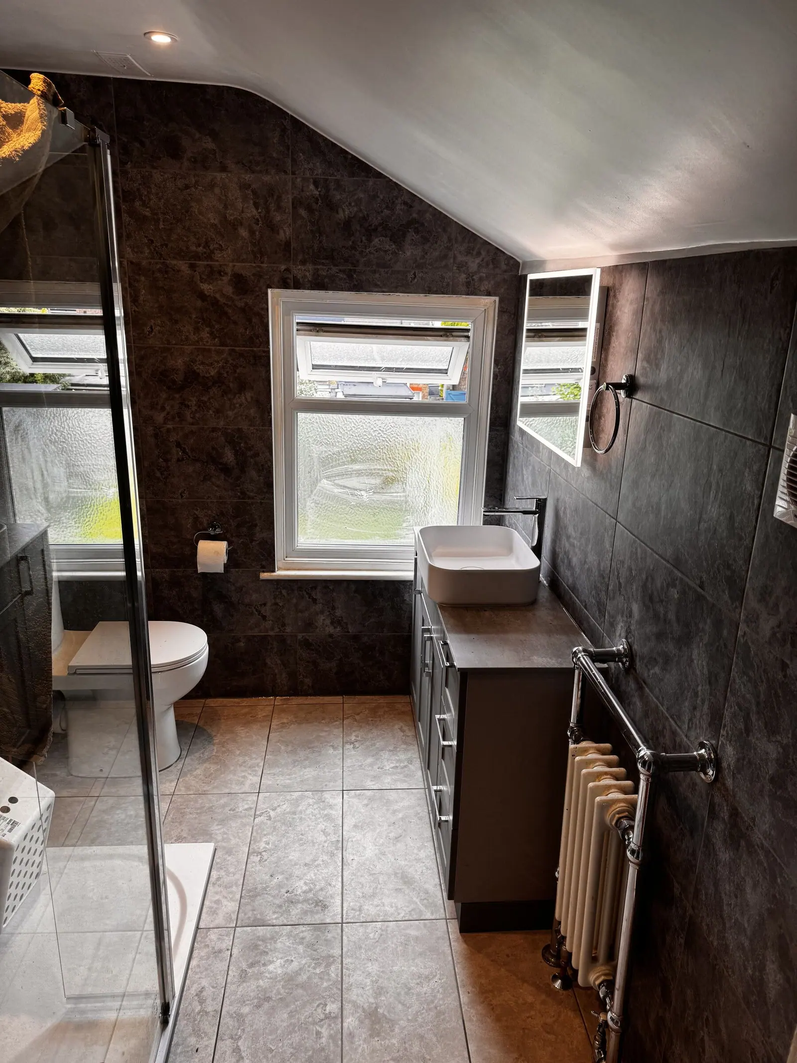 Loft shower room with dark stone-effect tiles, walk-in shower, grey vanity and a traditional radiator, fitted by Basingstoke Bathrooms